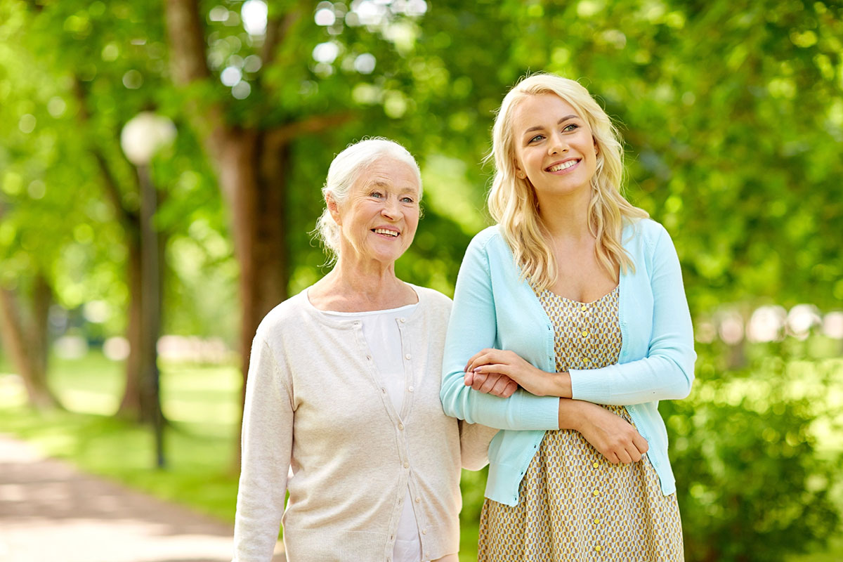 A senior woman is going for a walk in a park with a young woman by her side.