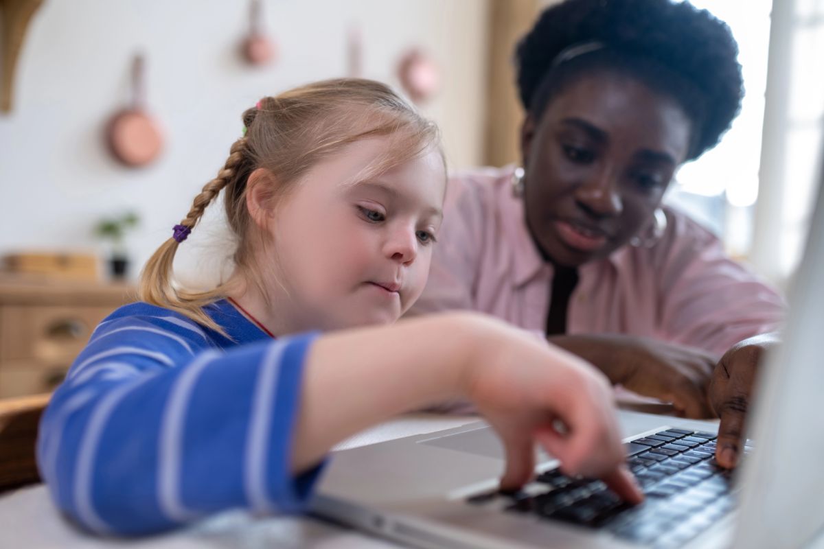 A teacher showing a child how to use a laptop.