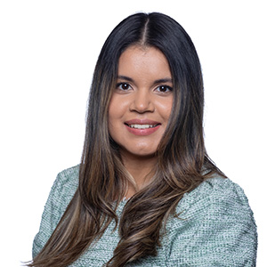 A smiling woman with long, dark hair, wearing a light green textured blazer, poses against a plain white background.